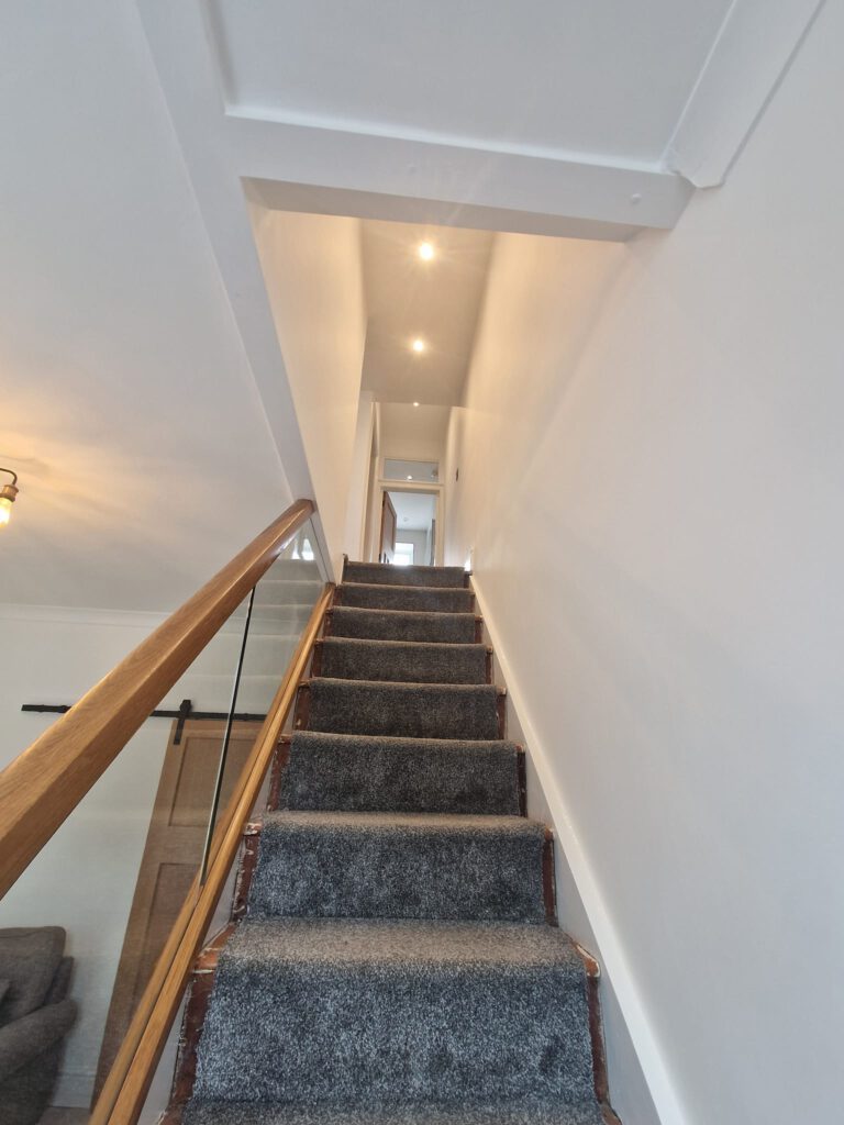 Staircase with white walls and an oak and glass balustrade