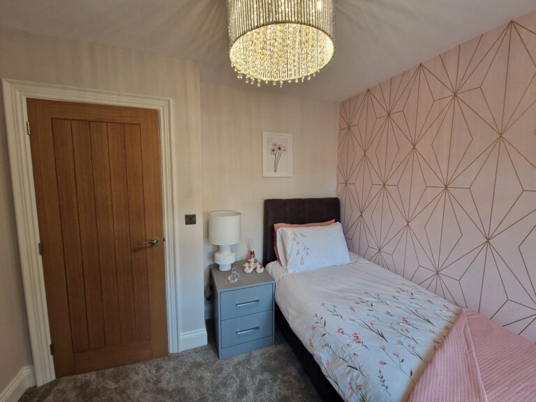 Bedroom with blush pink geometric wallpaper and an oak door